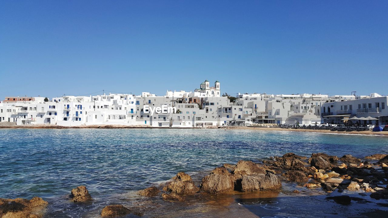 Sea by buildings against clear blue sky