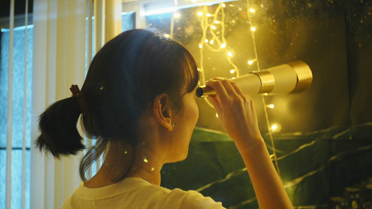 Rear view of woman looking through telescope at home