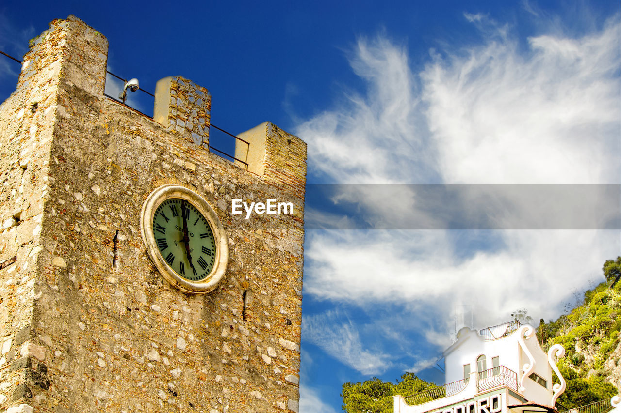 LOW ANGLE VIEW OF CLOCK AMIDST BUILDINGS AGAINST SKY