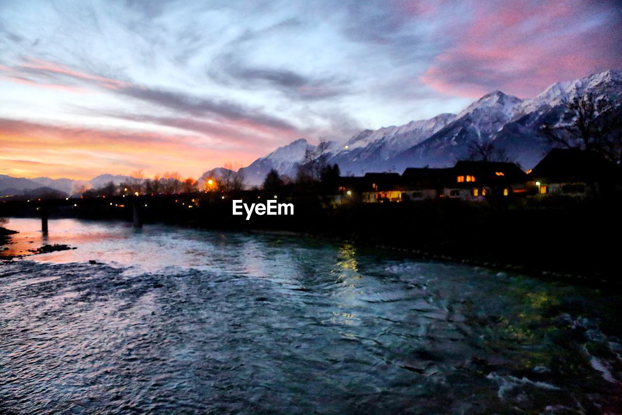 Scenic view of river by snowcapped mountains against sky during sunset