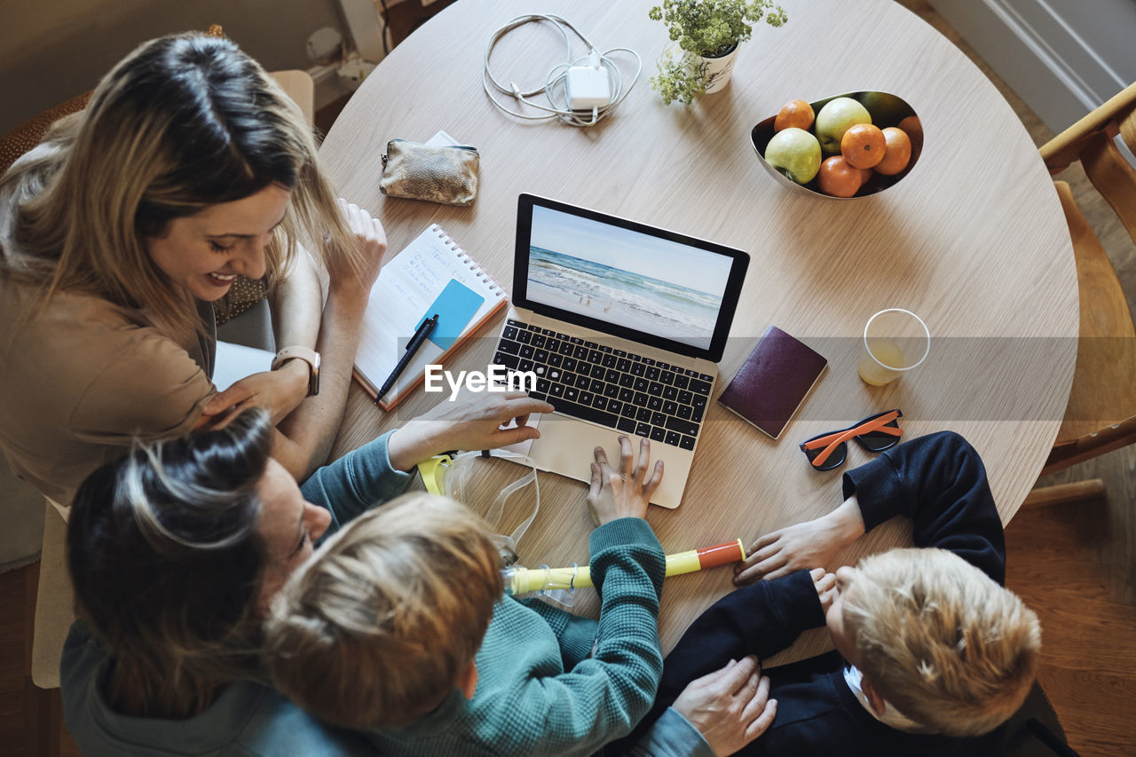 Directly above view of lesbian women planning vacation with sons on laptop at home