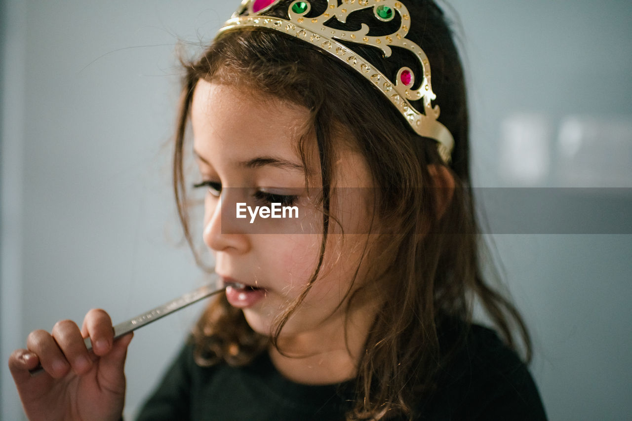 4 year old girl wearing tiara and eating from measuring spoon