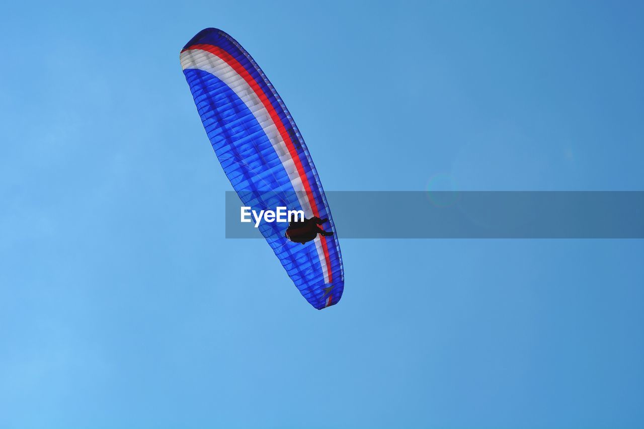 Low angle view of man paragliding in blue sky