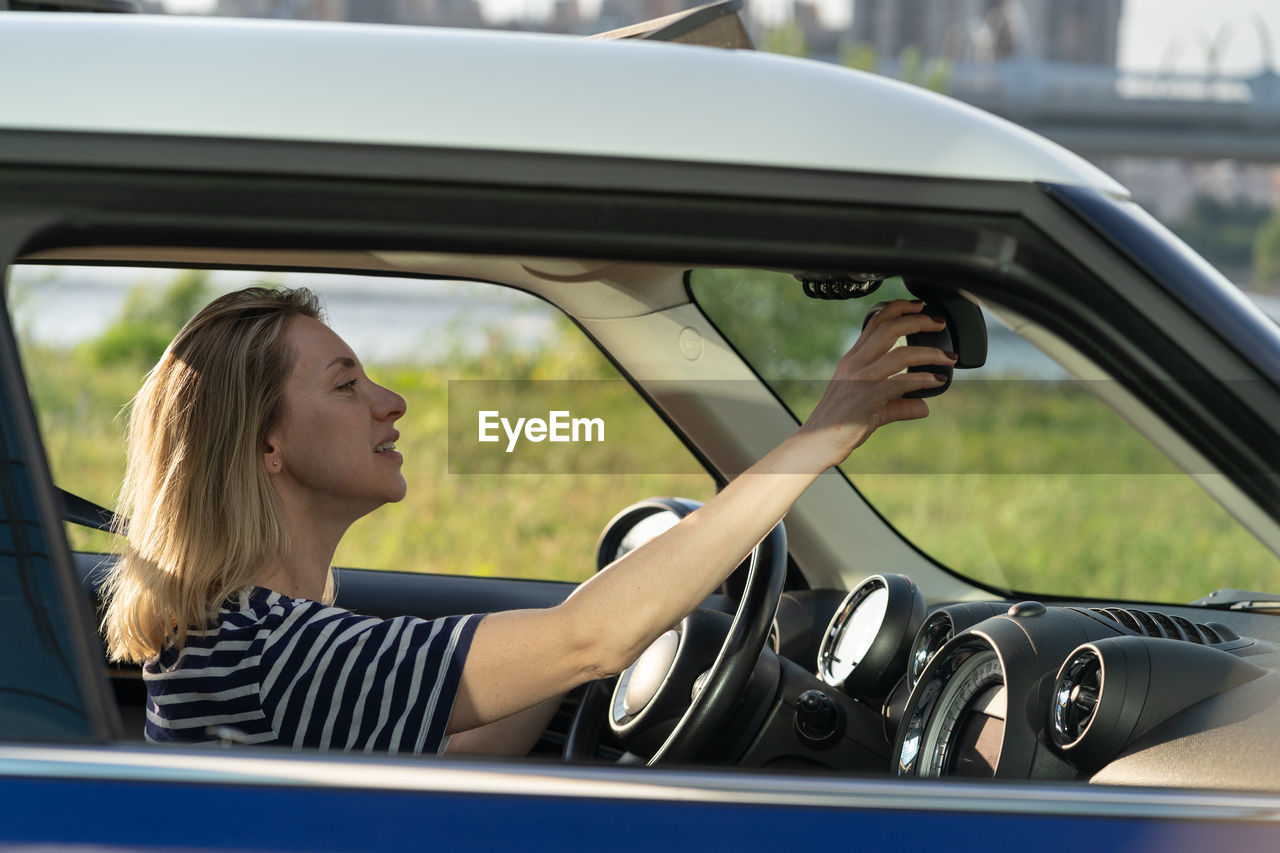 Woman adjusting rear view mirror of car