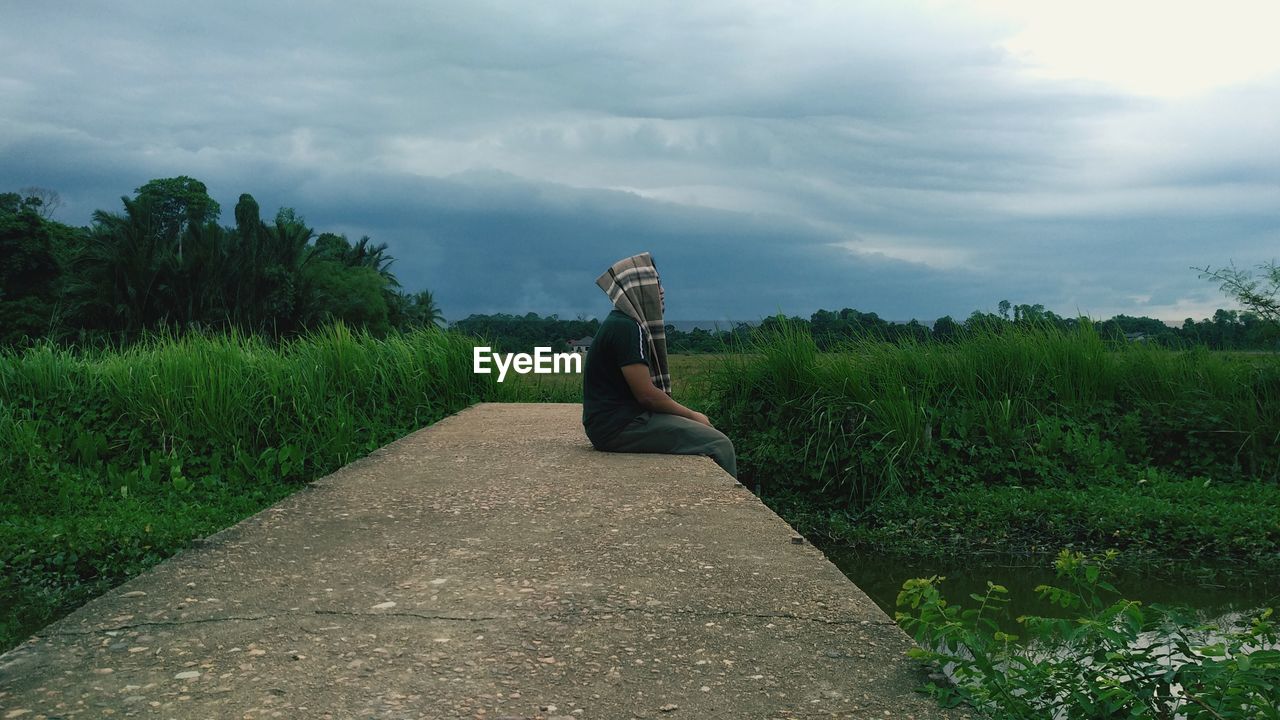 Side view of man sitting on field against sky