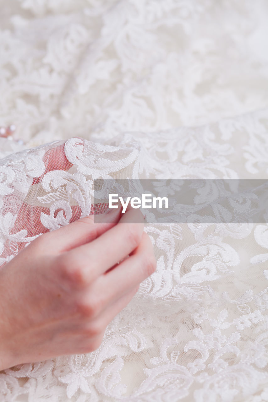 Cropped hand of woman stitching pearls on white wedding dress