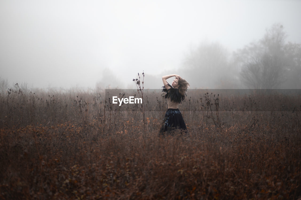 Woman standing on field by trees against sky