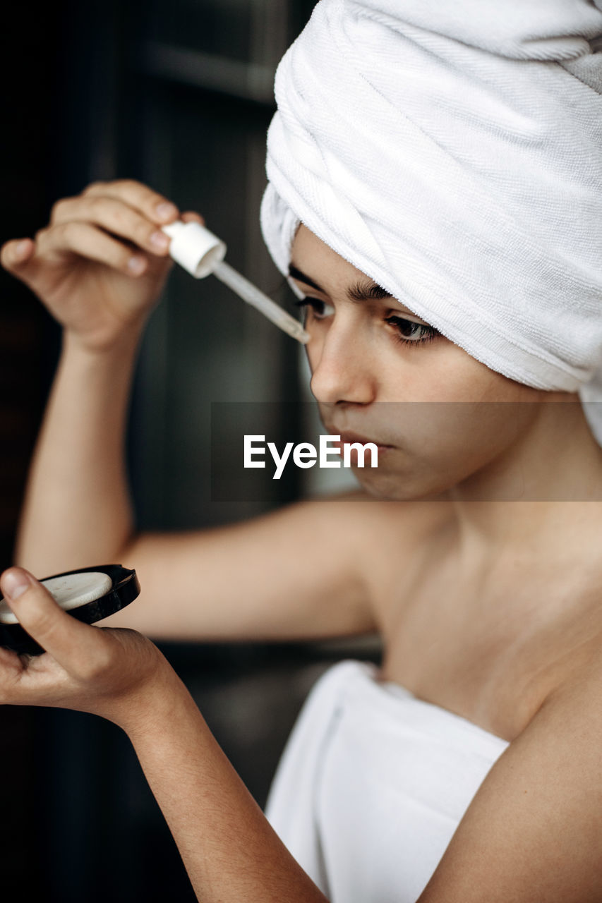 Young girl with towel on head makes facial treatments. skin care, moisturizing with serum