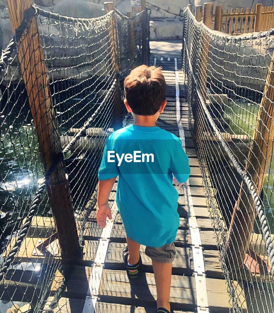 Rear view of boy walking on footbridge over river