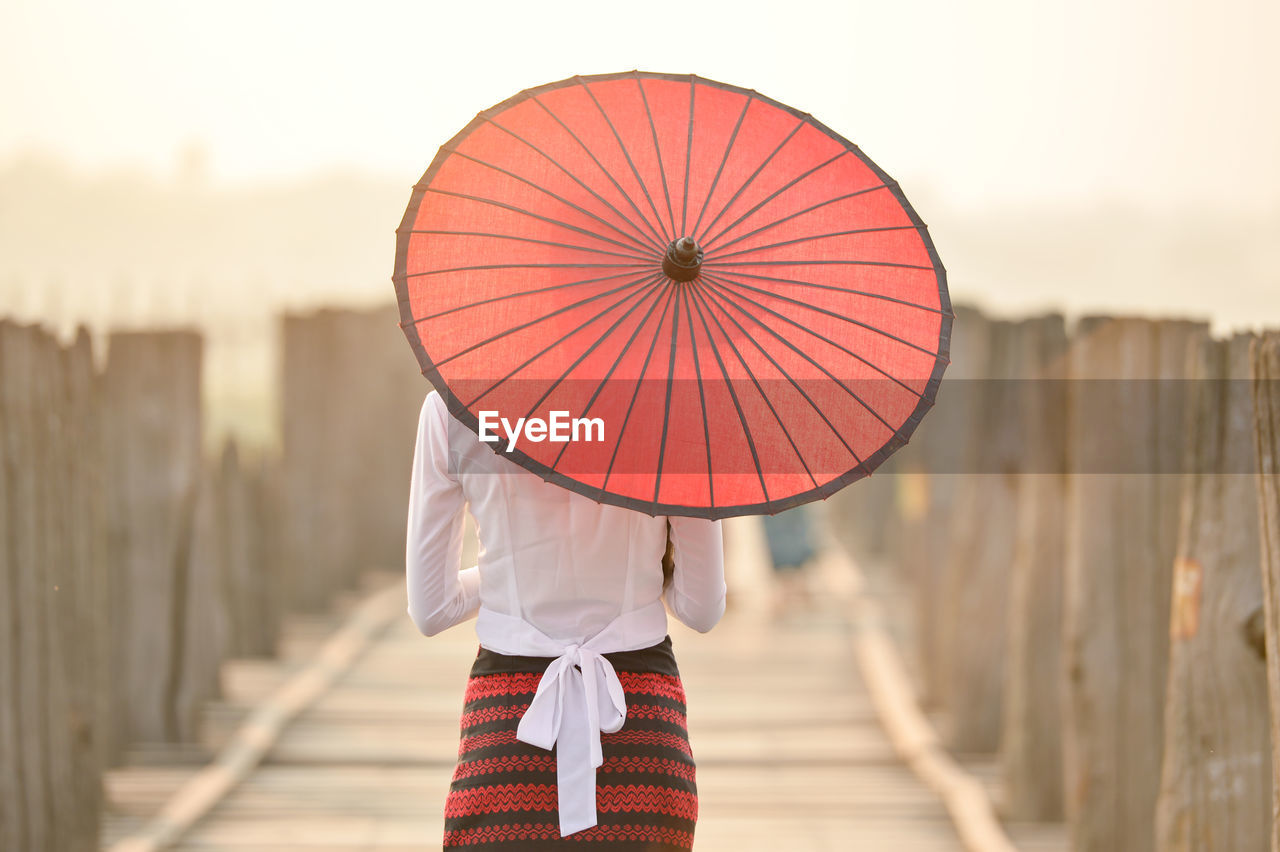 Burmese woman in  traditional costume holding red paper umbrella,