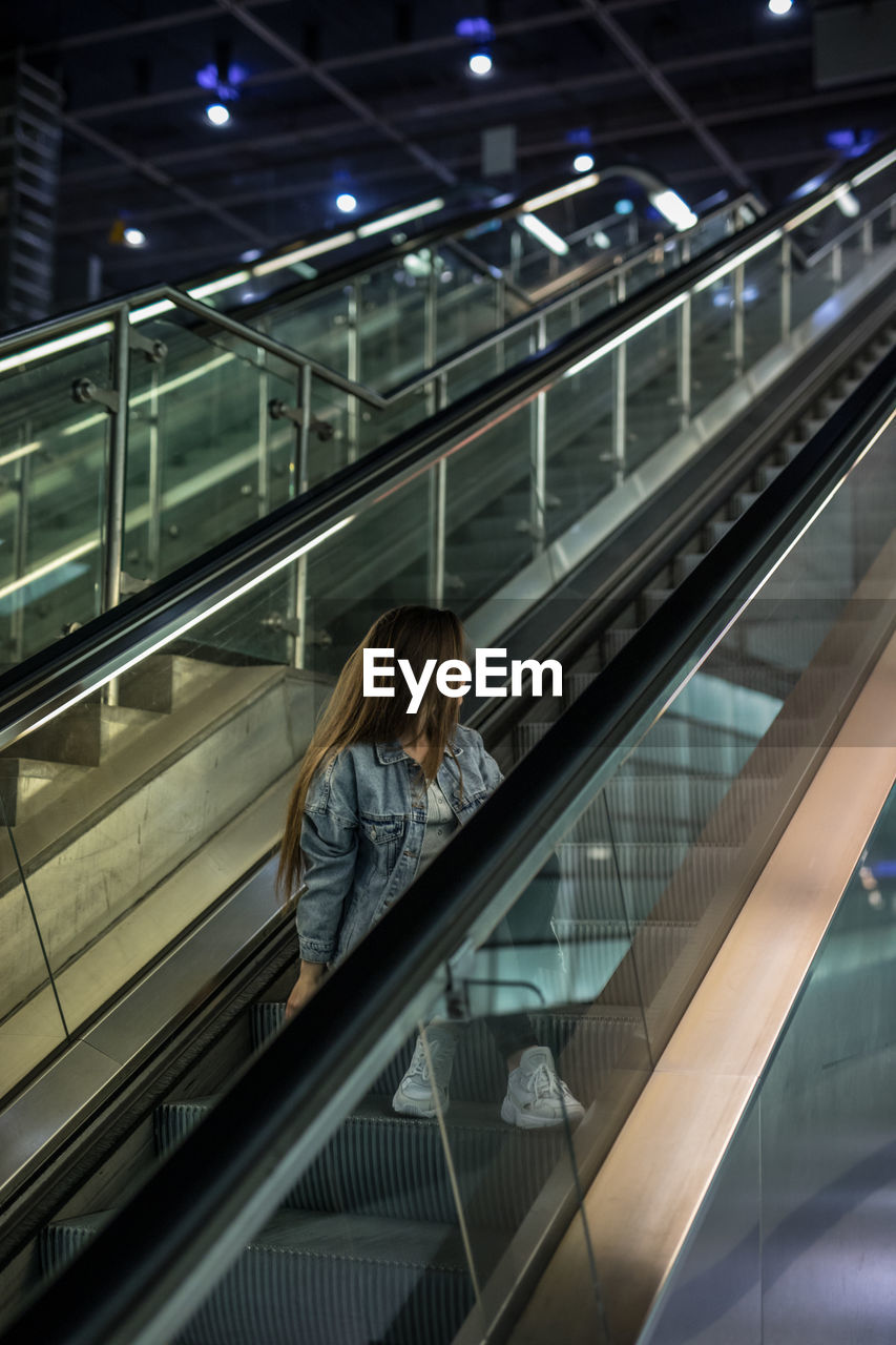 Full length of woman looking away while sitting on escalator