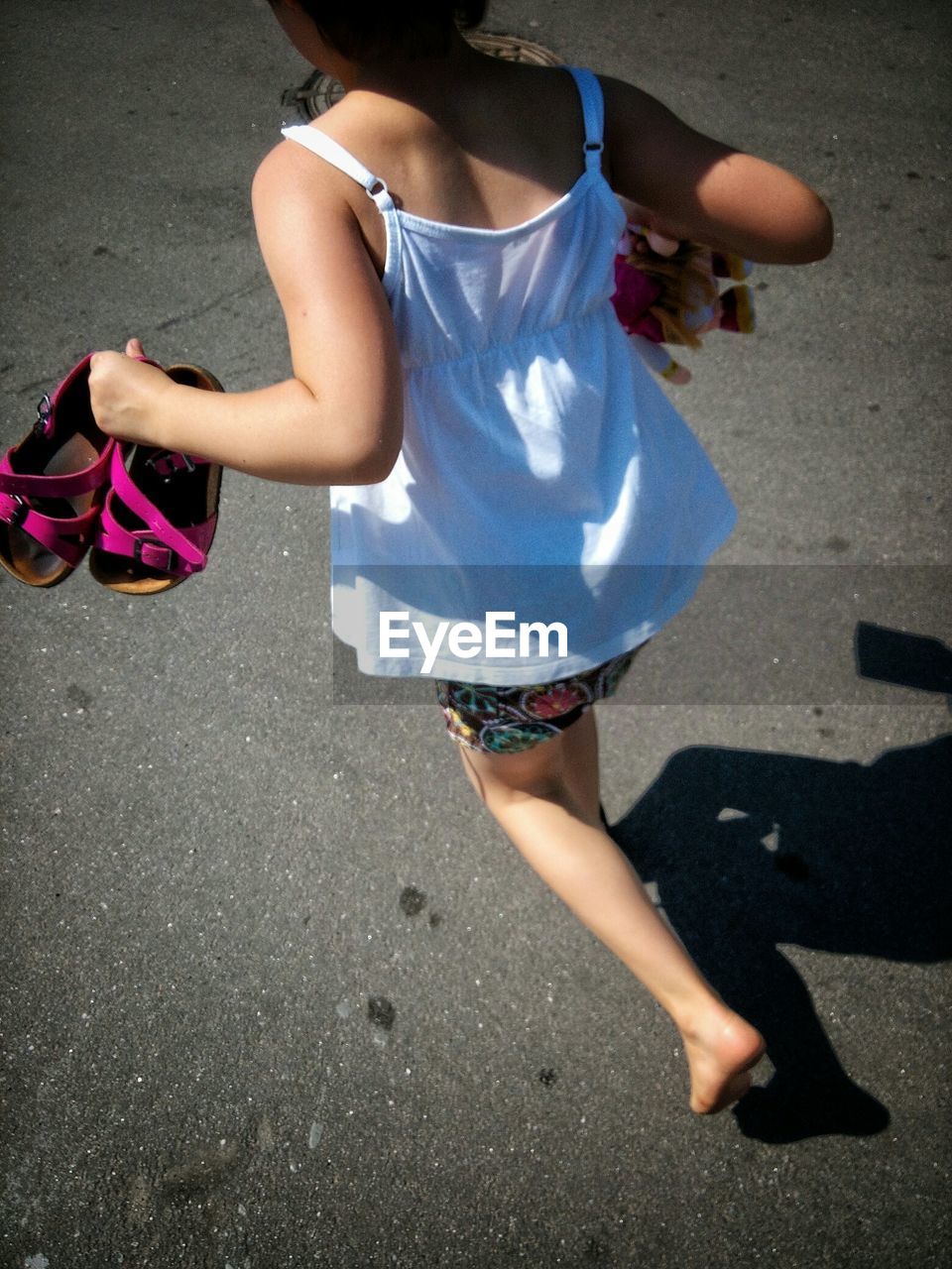 Low section of girl holding shoes while walking on street