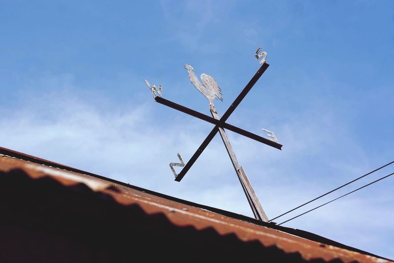 Low angle view of weather vane on house against sky