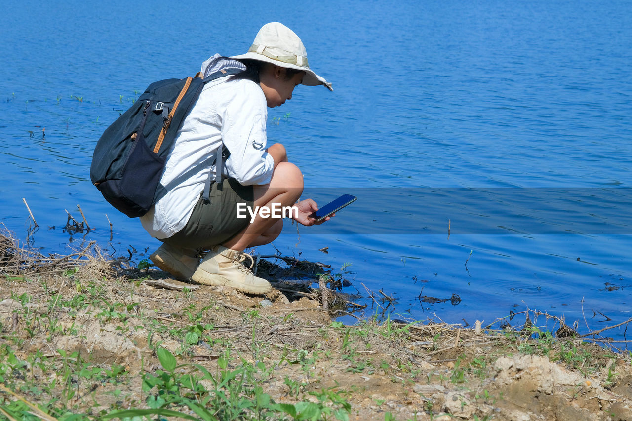 rear view of woman sitting on rock by lake