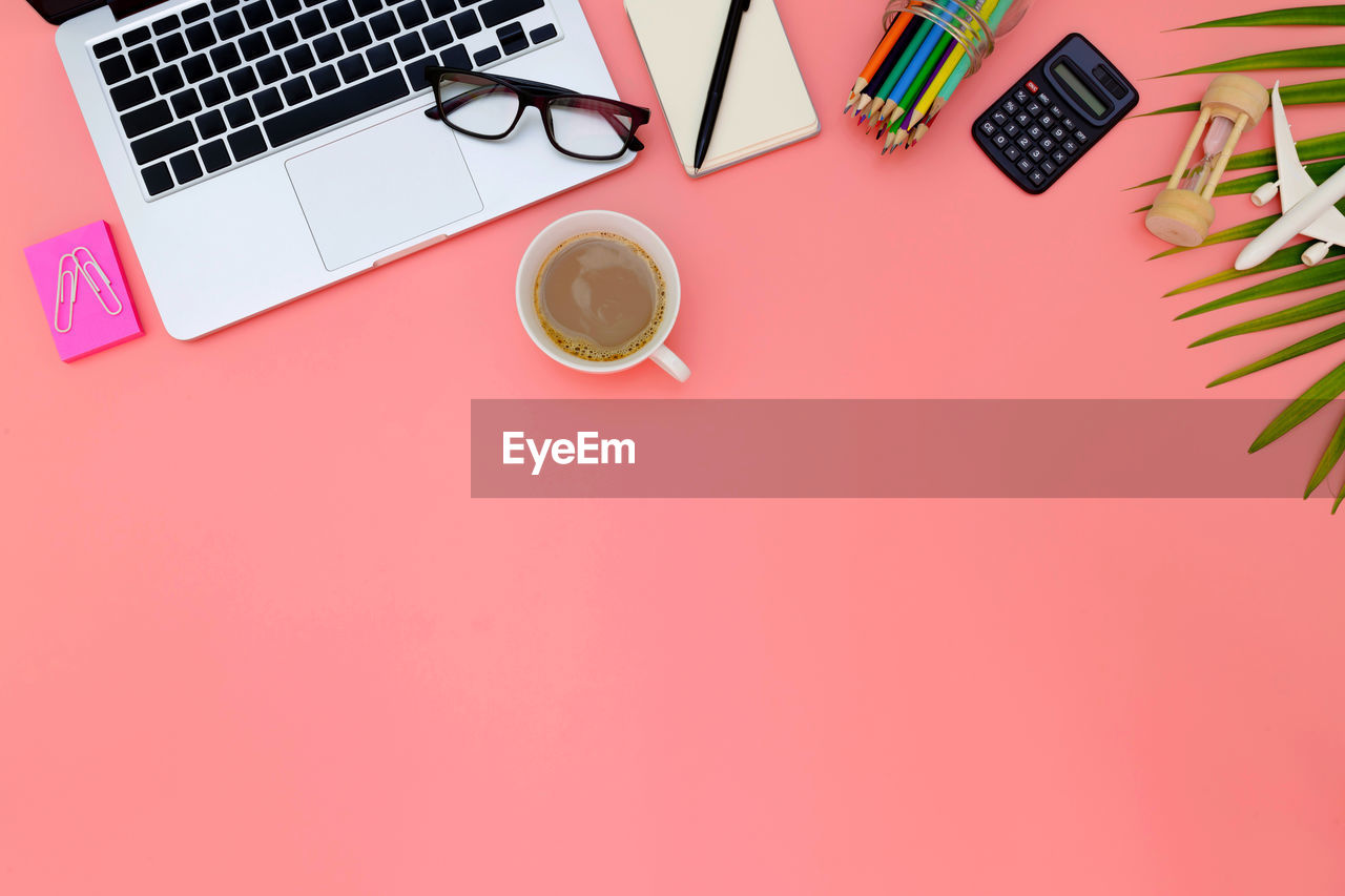 Directly above shot of laptop with coffee and various objects on pink background