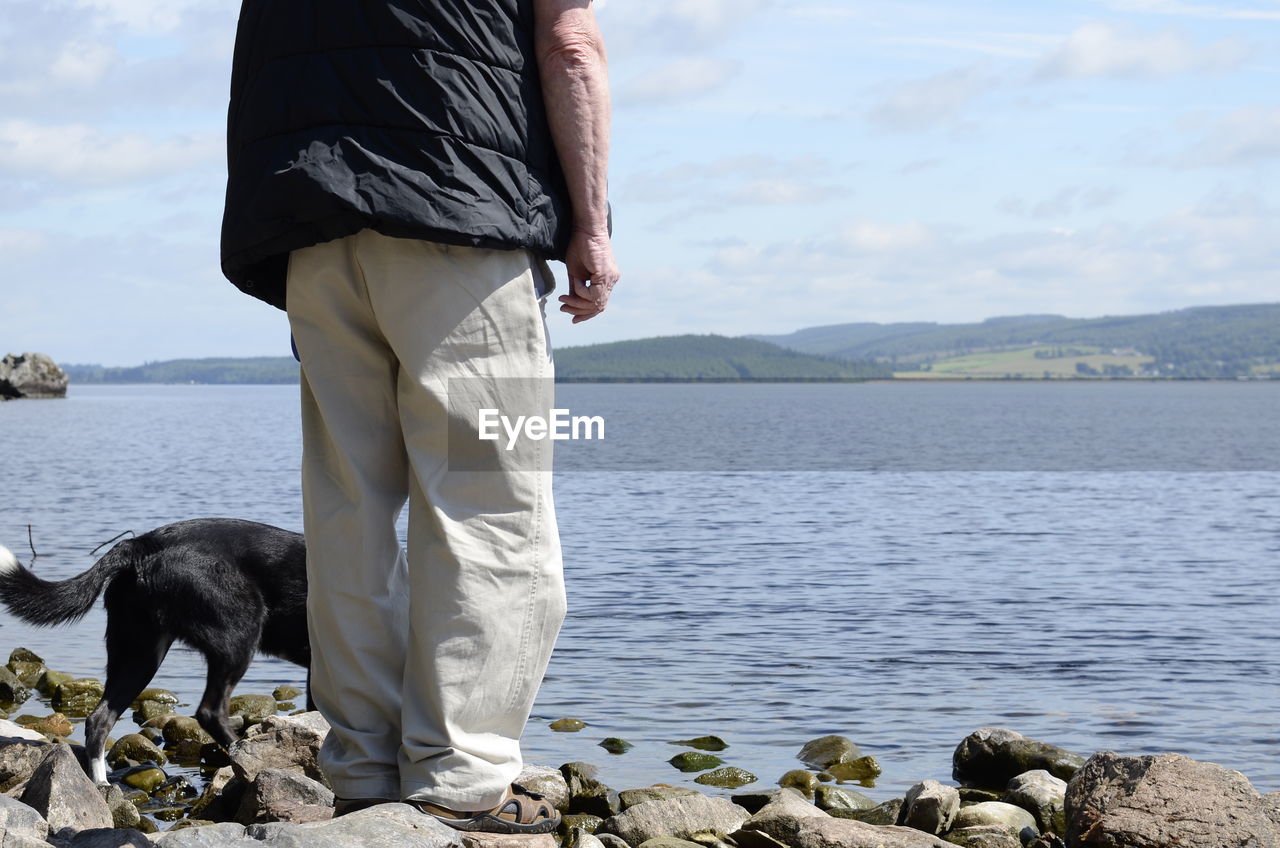 LOW SECTION OF MAN STANDING ON SEA SHORE