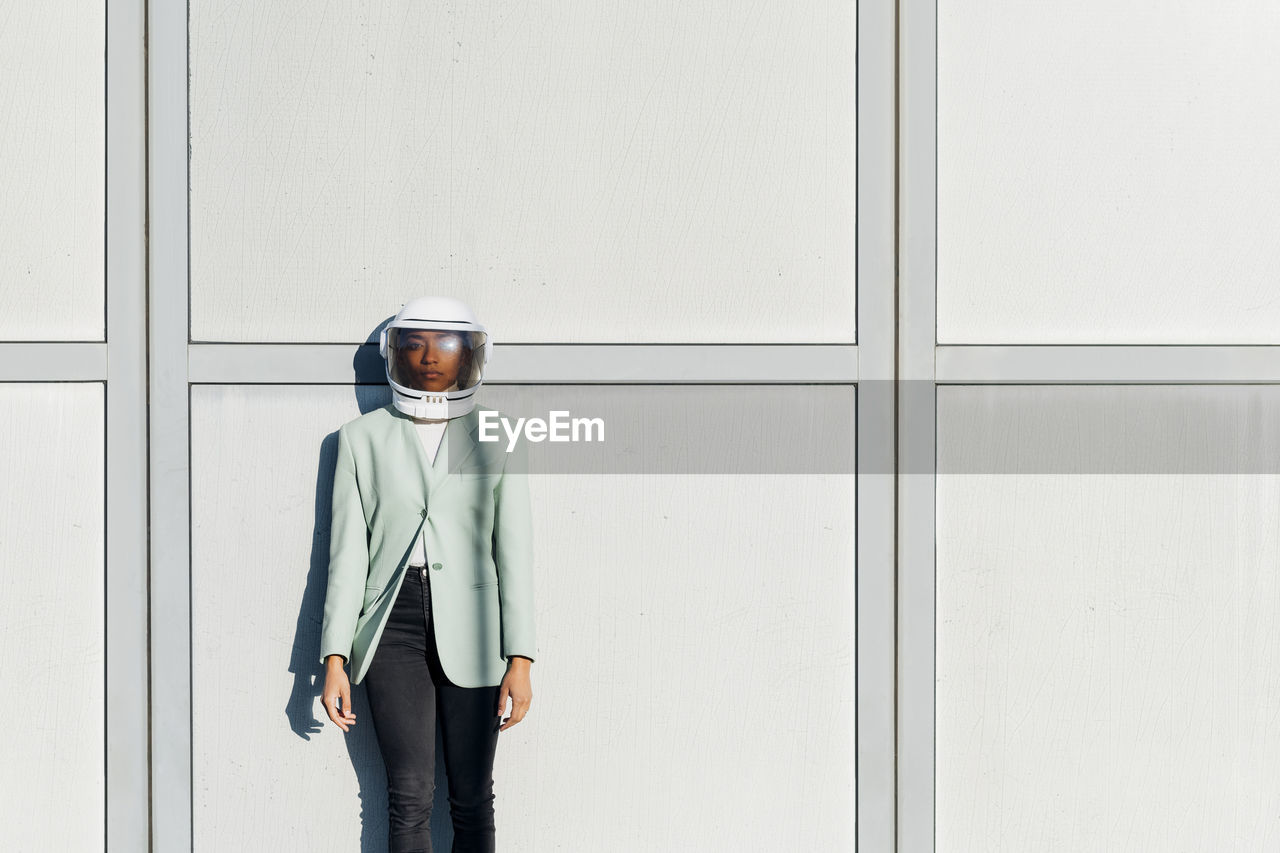 Young businesswoman wearing astronaut helmet in front of wall