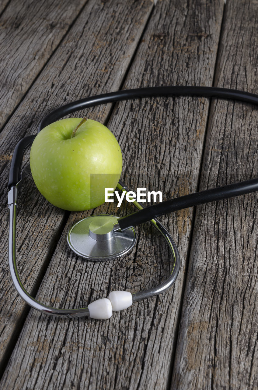 Stethoscope with fresh green apple on wooden table.