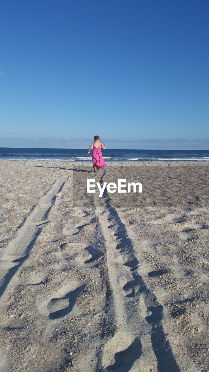 Rear view of girl walking on beach against clear sky