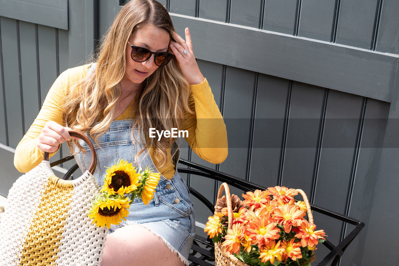 Young woman sitting by flowers against wall