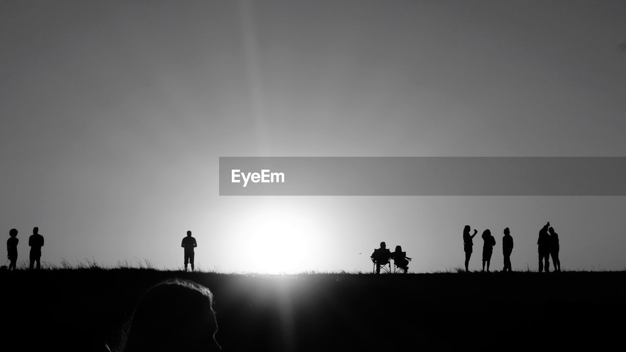 Silhouette people standing on field against clear sky during sunset