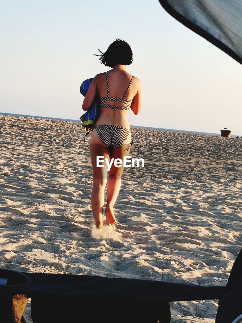 Rear view of woman in bikini walking on beach against sky