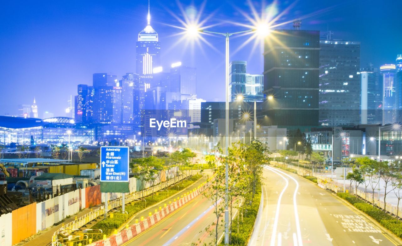 Illuminated street light amidst road against buildings