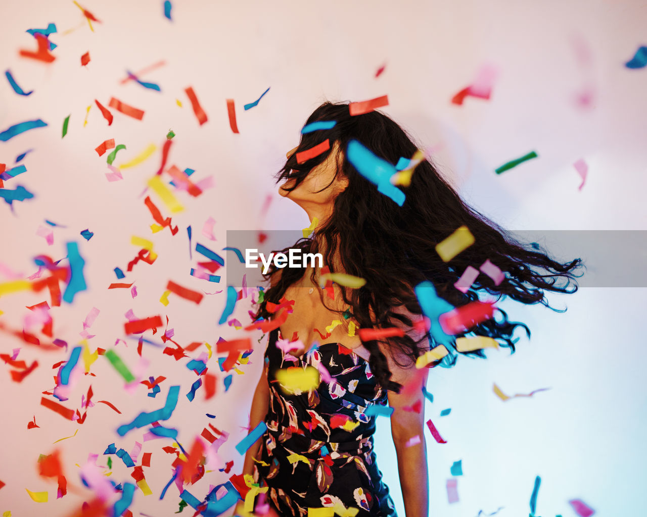 Colorful confetti against young woman standing by wall