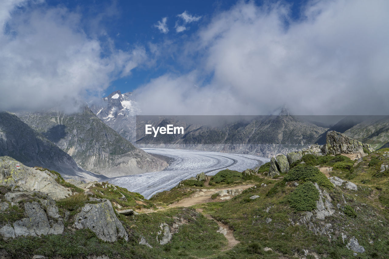 Snow covered road amidst mountains against cloudy sky