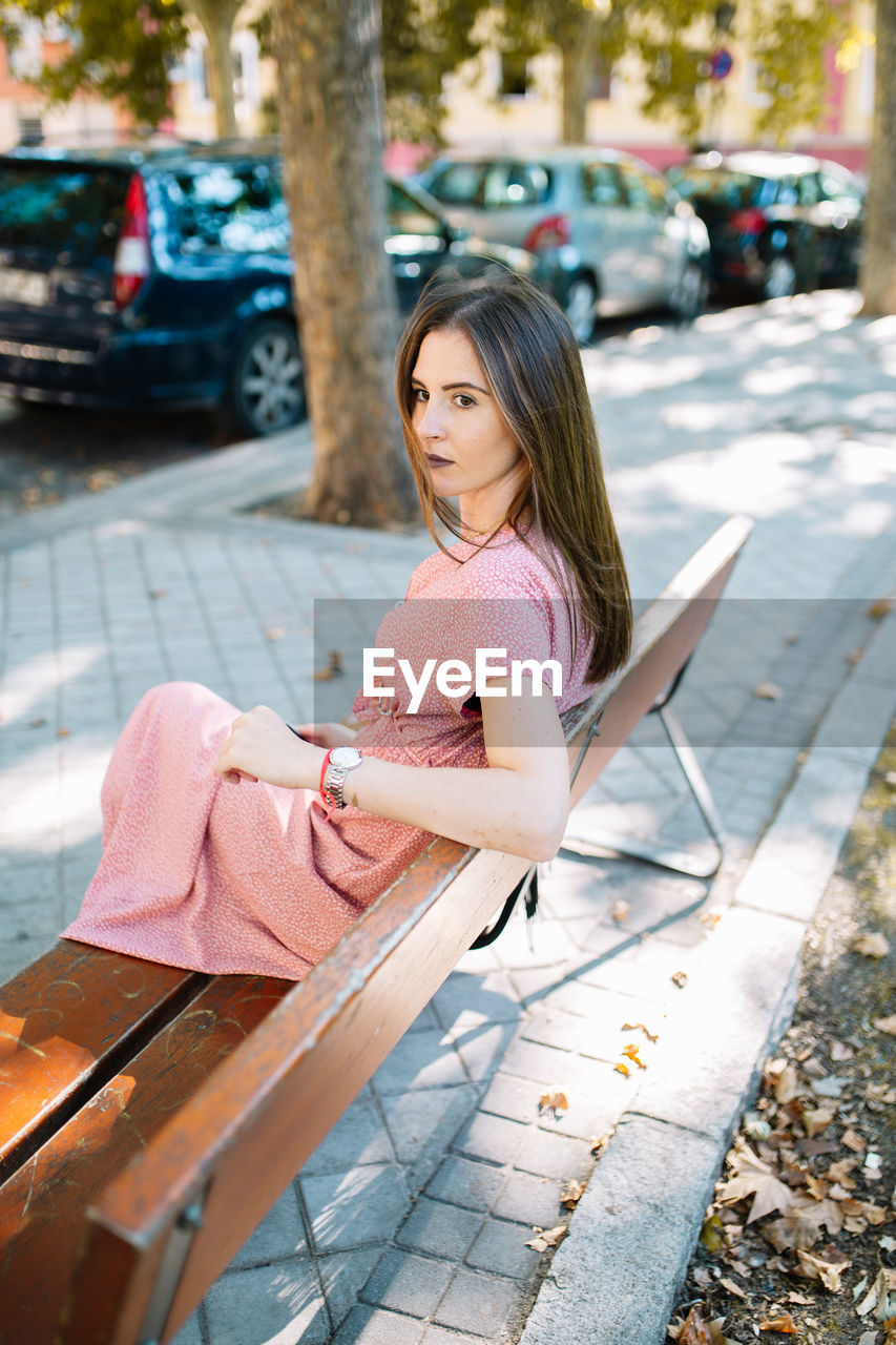 Thoughtful young woman sitting on bench at sidewalk