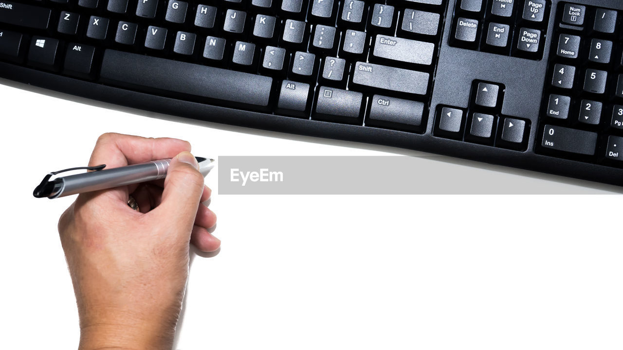 Cropped hand of person holding paper by keyboard on table