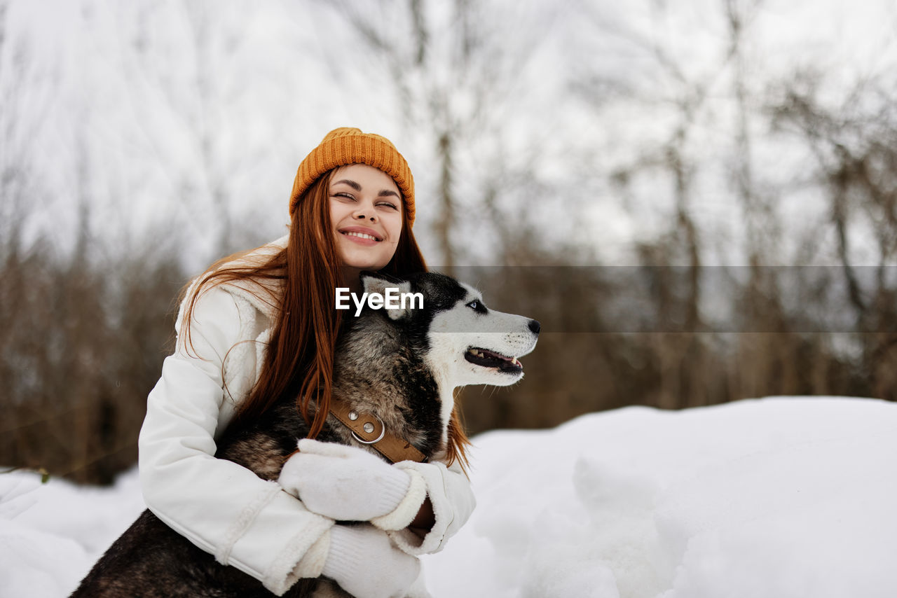 Smiling woman with dog on snow covered field
