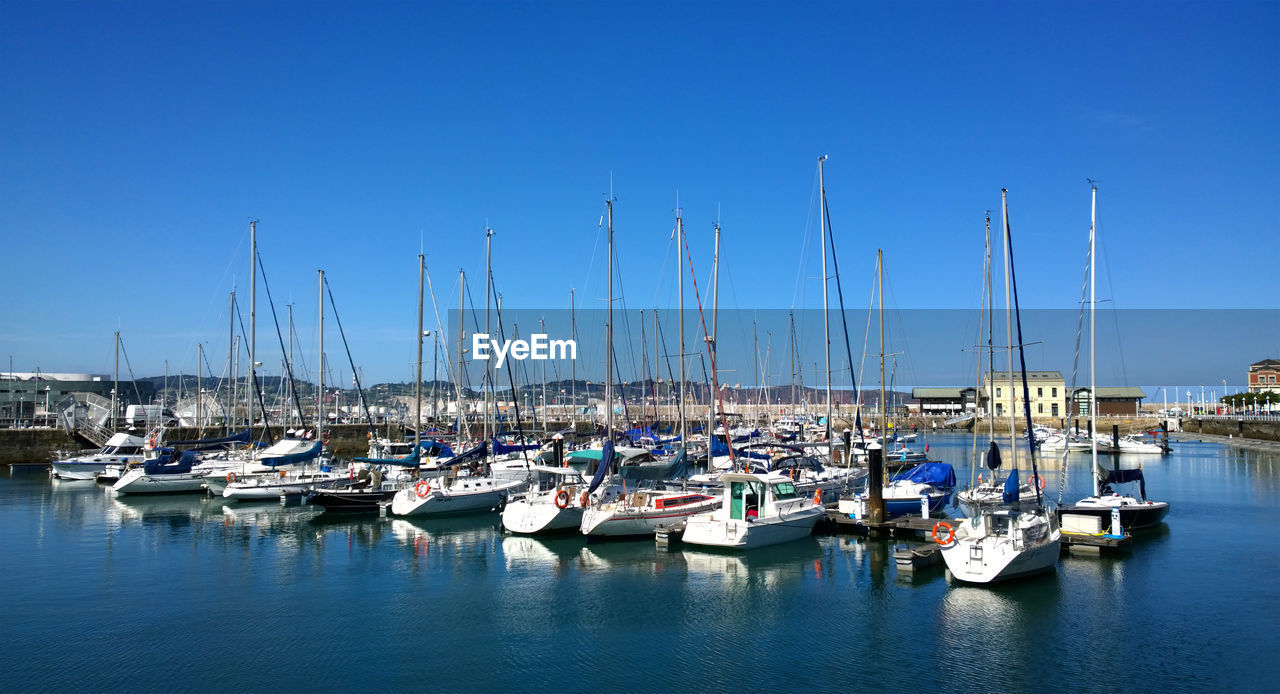 Sailboats moored in harbor against clear blue sky