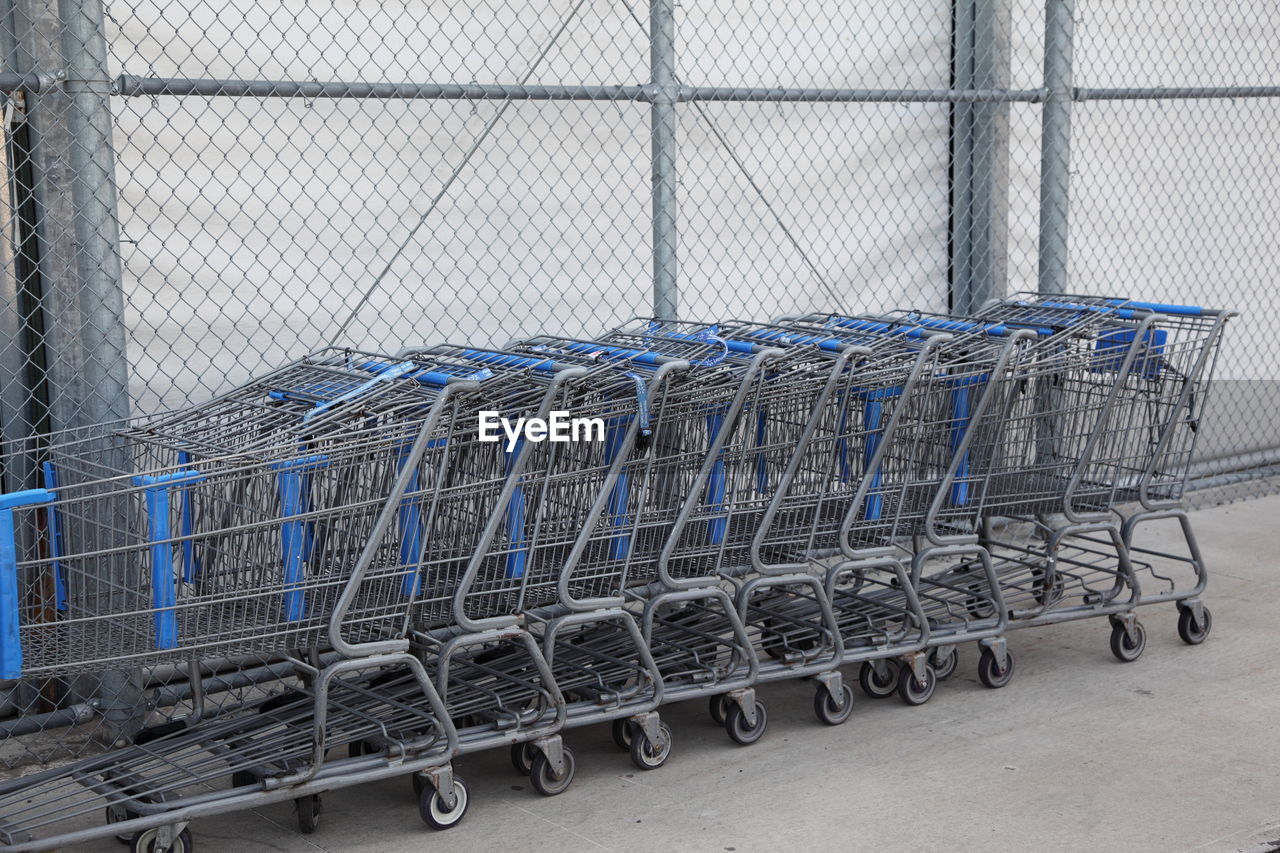 Shopping carts arranged in row against chainlink fence