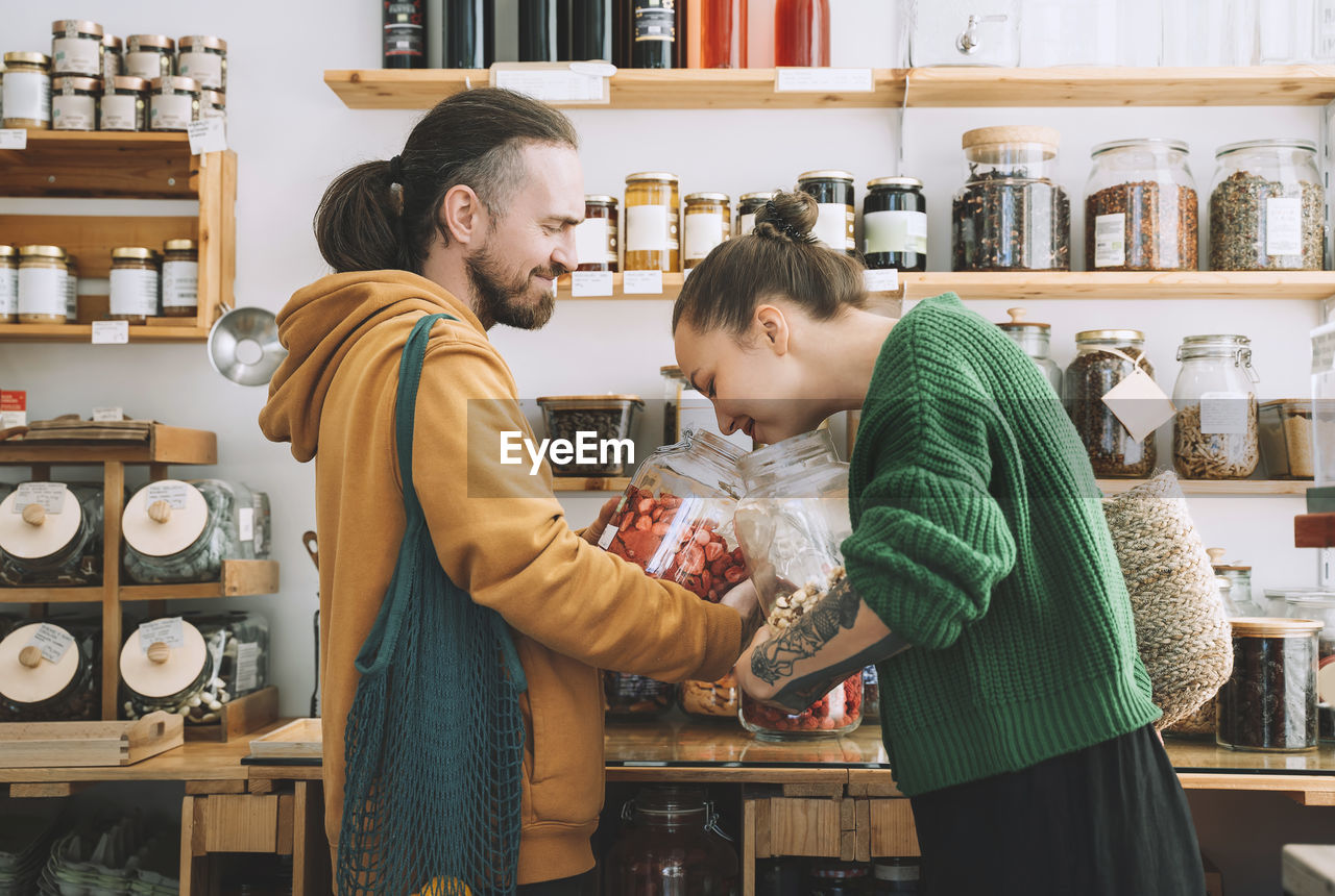 Woman smelling dried strawberries with man holding jar at store
