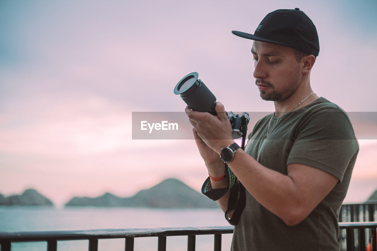 Male photographer with green t-shirt and black flat cap looking at his camera with a  telephoto