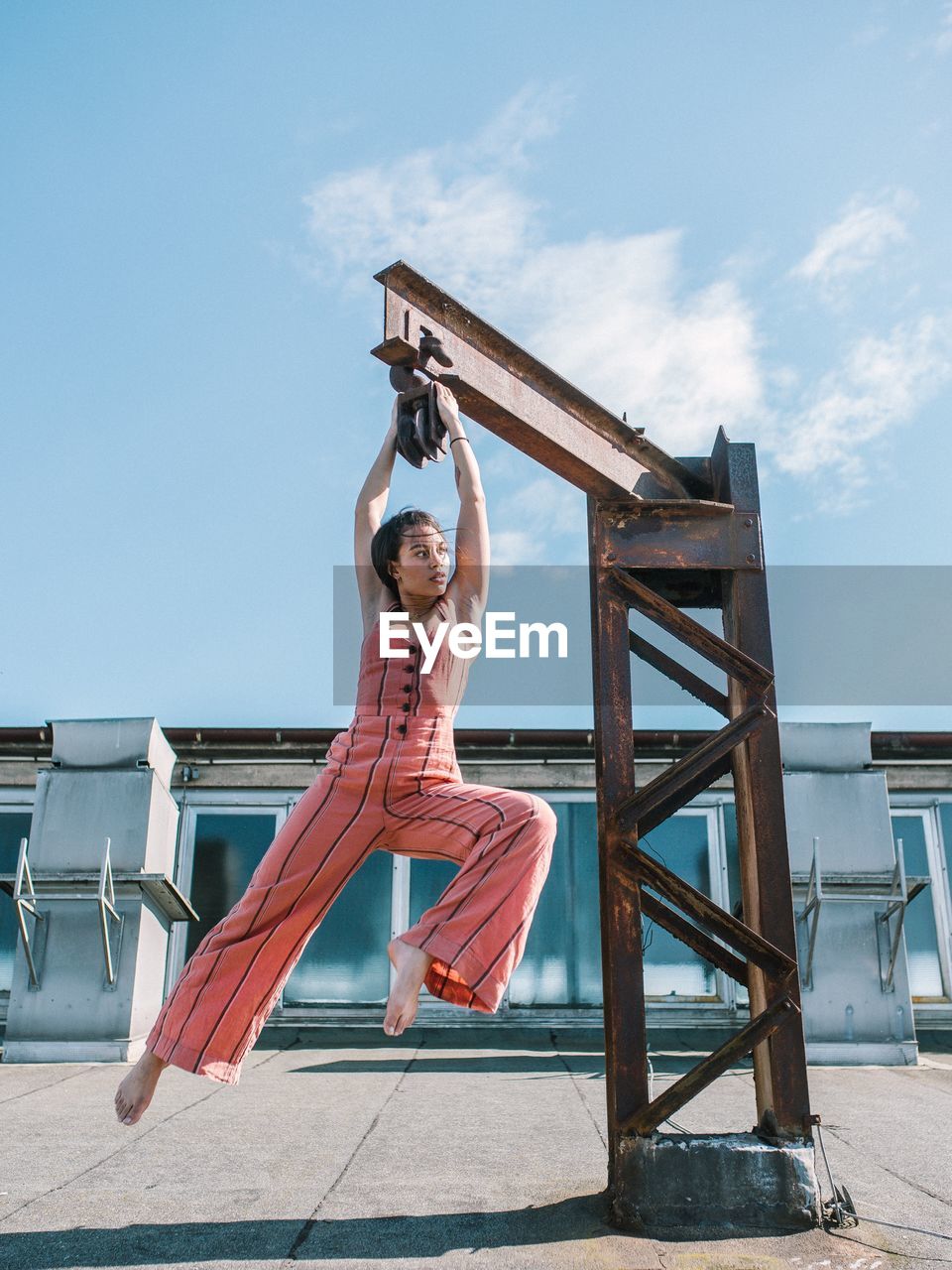 Woman hanging from metal against blue sky