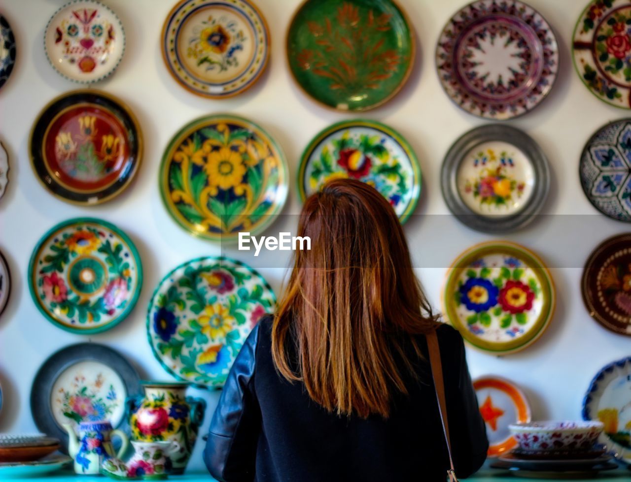 Rear view of woman standing against multi colored dishes on wall