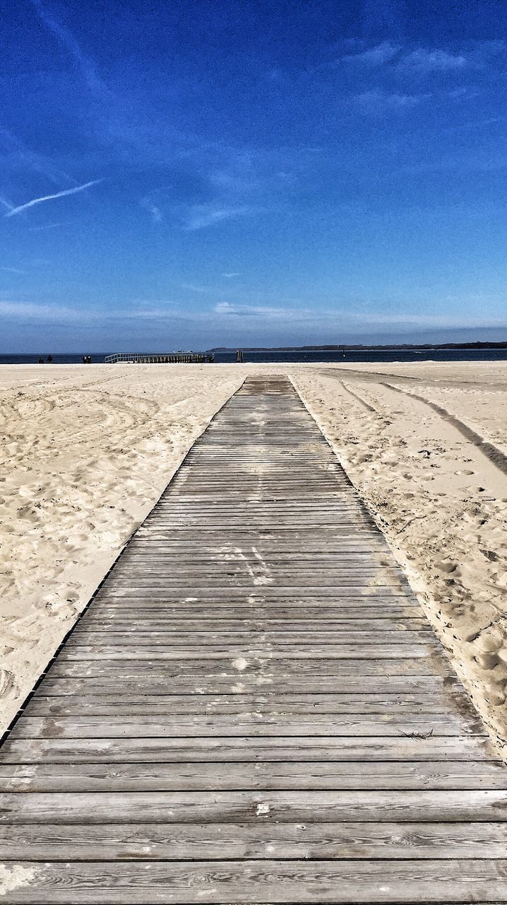 Wooden boardwalk on beach against sky during sunny day