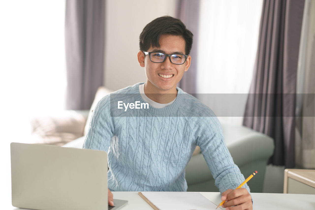 PORTRAIT OF SMILING YOUNG WOMAN USING LAPTOP