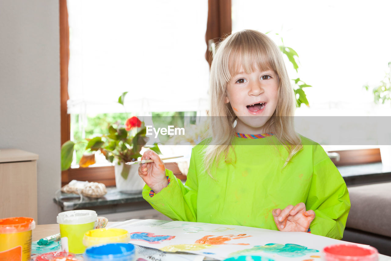 Portrait of girl painting on paper while sitting at home