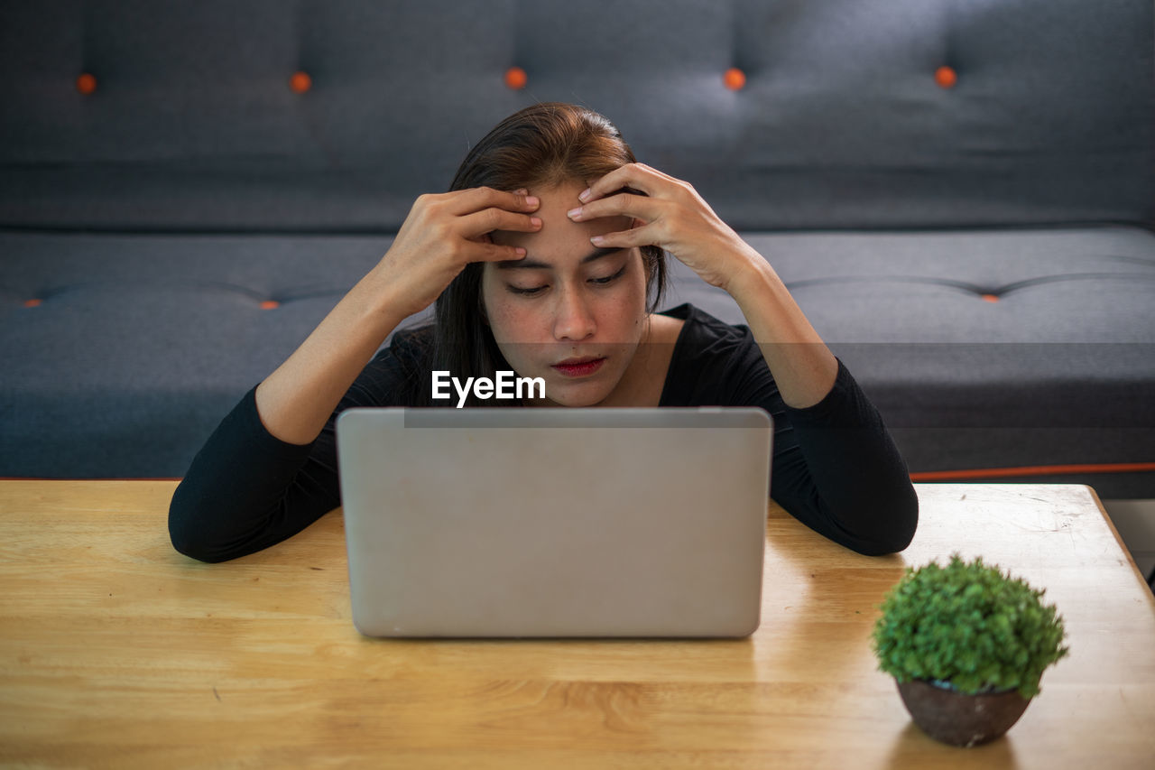 Woman with head in hands using laptop on table at home