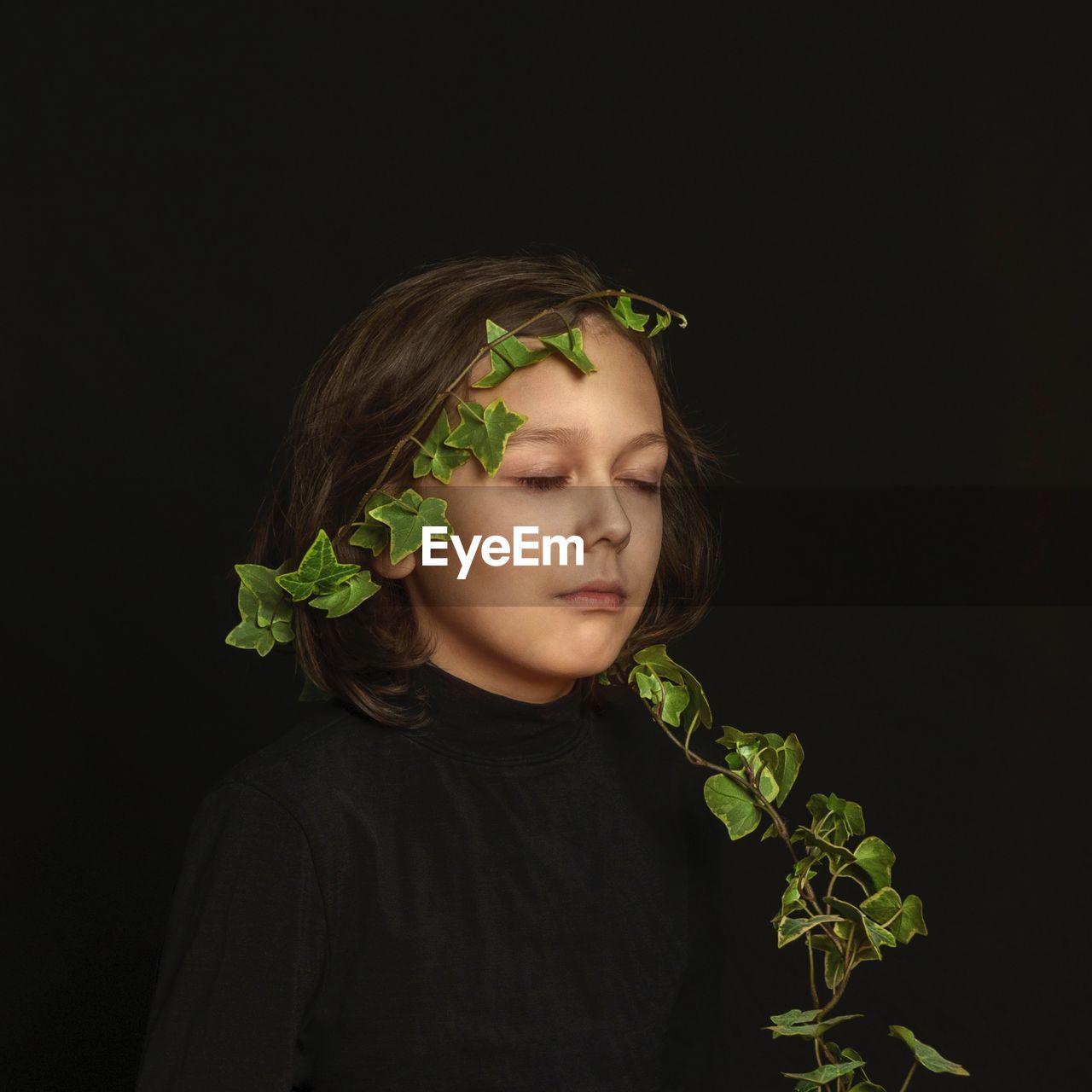 Portrait of a kid with a green plant against the black background