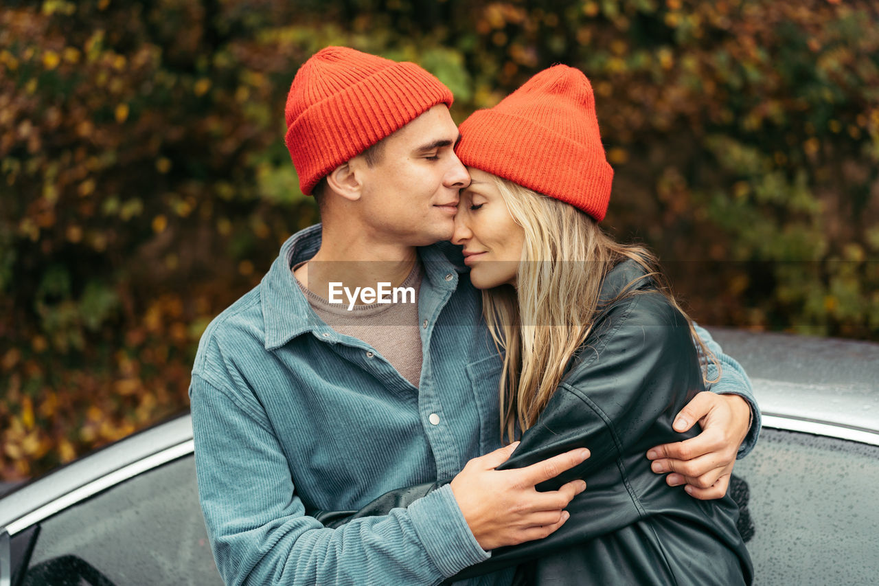 Young man and woman in red caps hugging outdoors in autumn.
