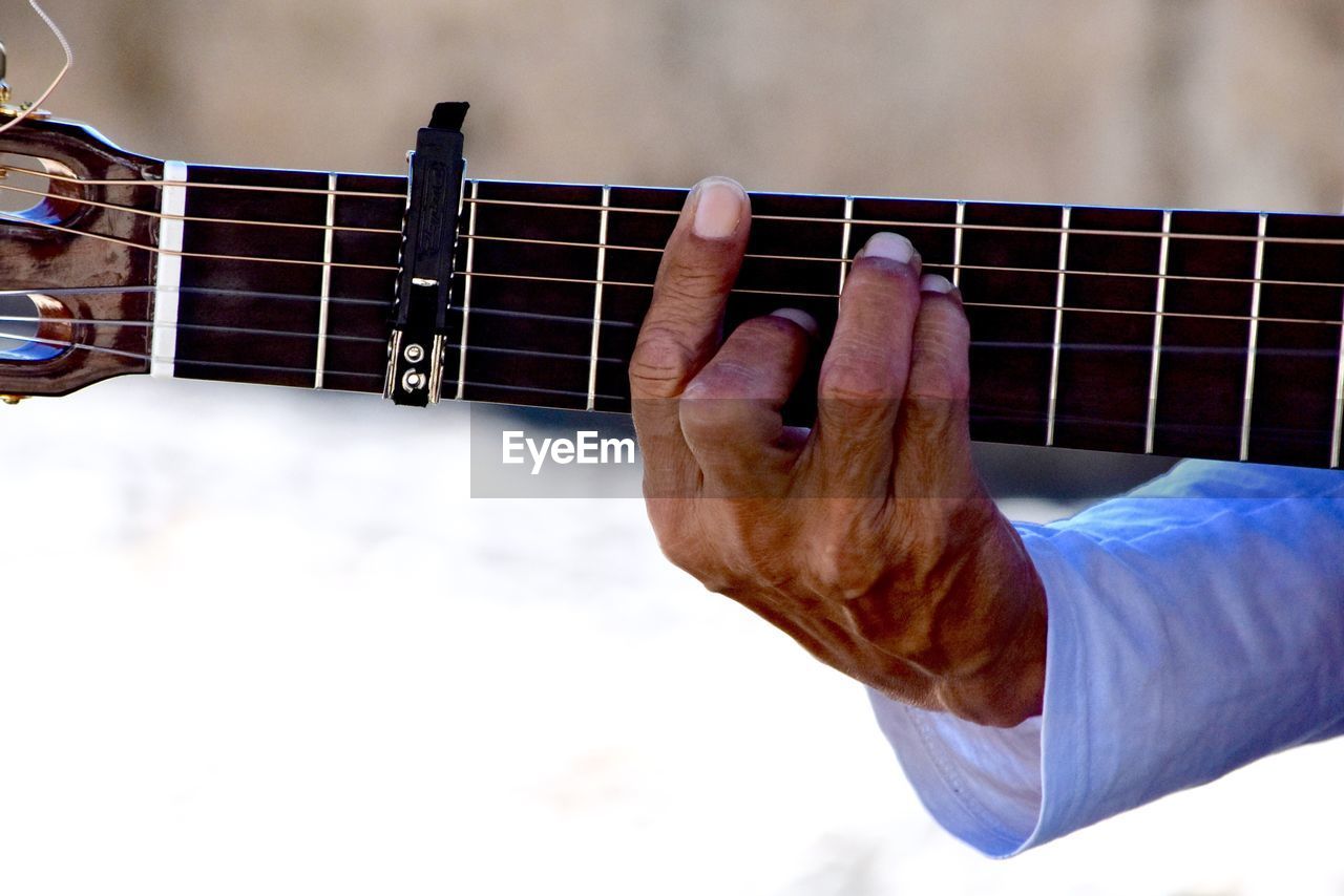 CLOSE-UP OF MAN PLAYING GUITAR AGAINST THE SKY