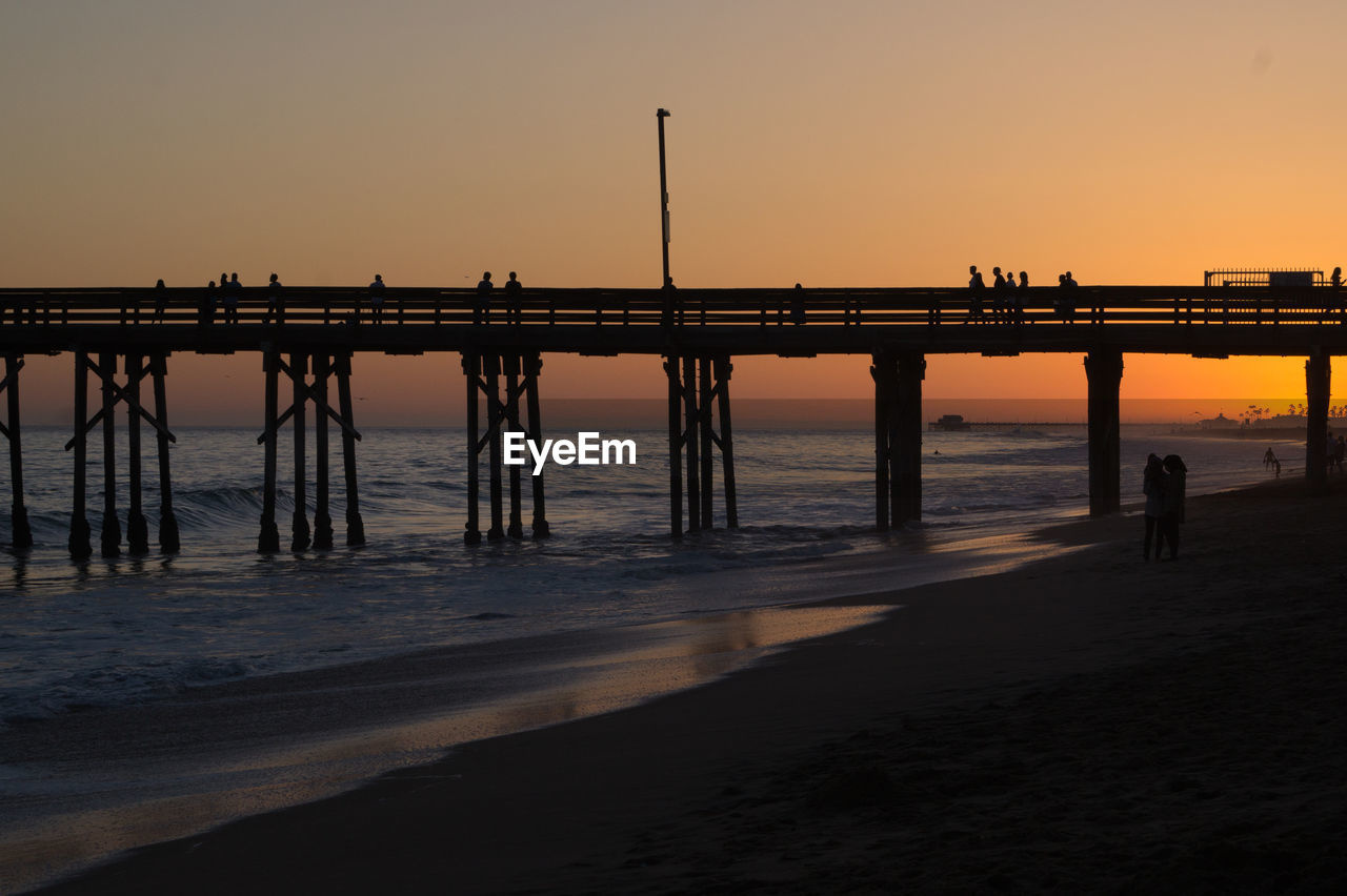 Silhouette pier on beach against clear sky at sunset