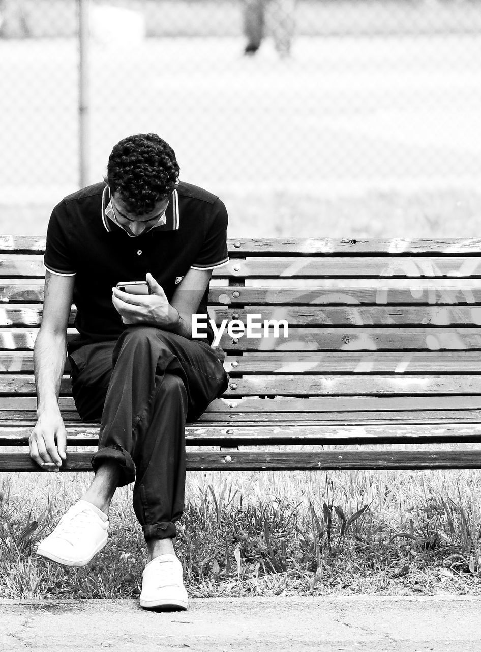 FULL LENGTH OF MAN SITTING ON BENCH IN PARK