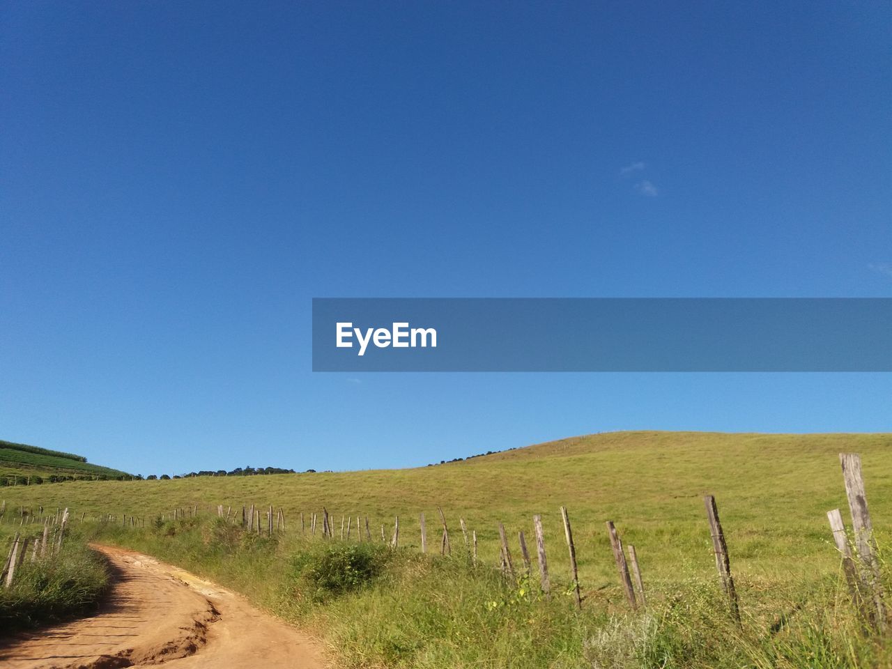 Dirt road amidst field against blue sky