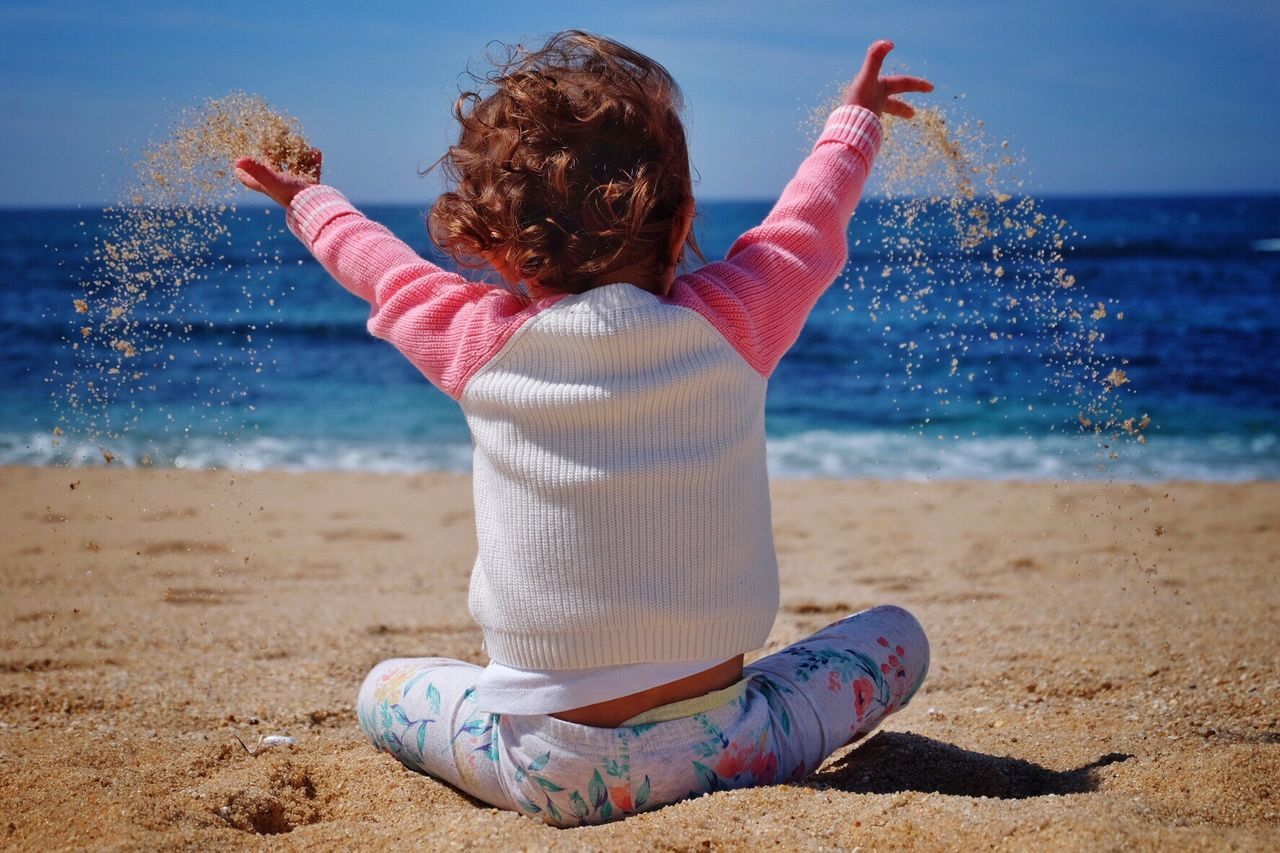 Rear view of child throwing sand at beach on sunny day