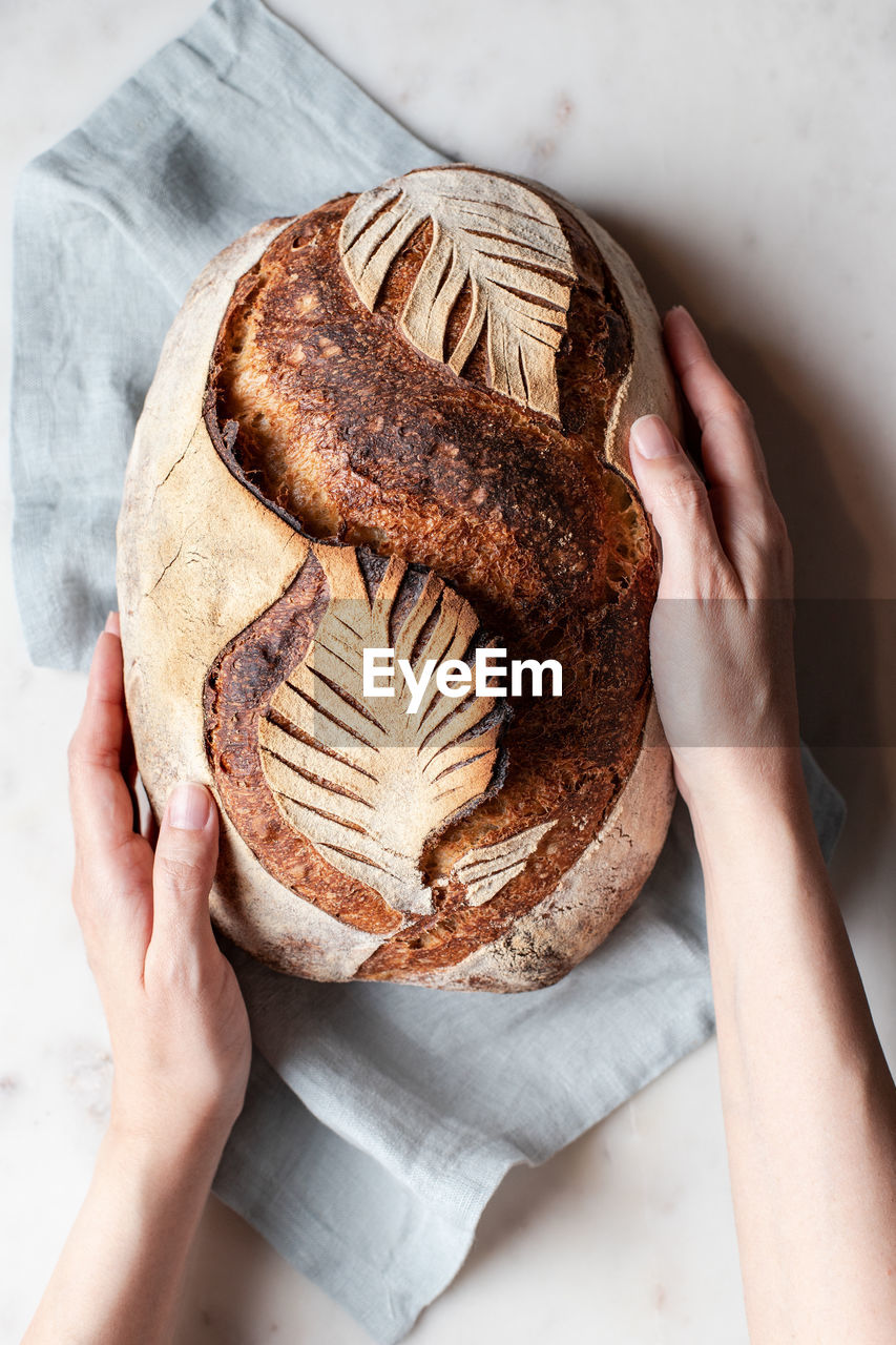 Top view of crop anonymous person with freshly baked bread with creative leaf pattern on white background in light kitchen person